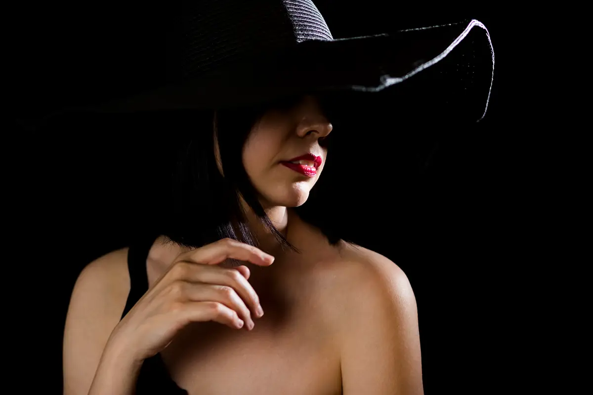 una ragazza con rossetto rosso fuoco, viso in ombra con focus sulle labbra e cappello nero