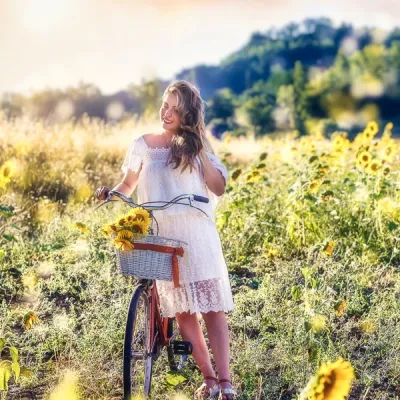 Servizi Fotografici Ritratto All Aperto Reggio Emilia - ragazza bionda in abito bianco fotografata in un campo di girasole con una bicicletta rossa ed un cestino colmo di fiori